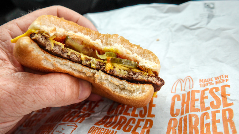 A hand holding a McDonald's cheeseburger.