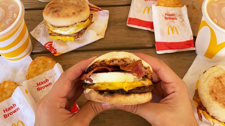 Hands holding a Sausage & Egg McMuffin with bacon.