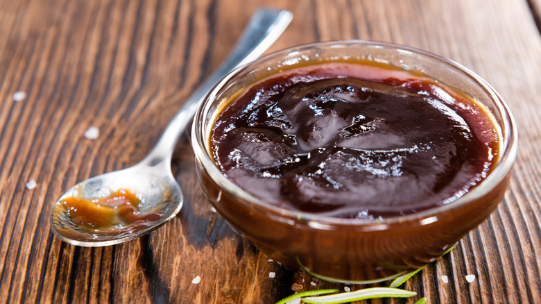 A bowl of barbecue sauce on a wooden table with a spoon.