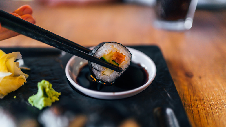 Sushi being dipped in bowl of soy sauce