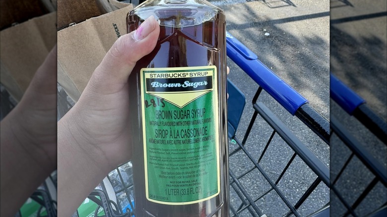 A hand holds a bottle of brown sugar syrup from Starbucks.