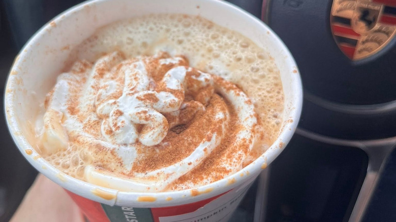 A hand holds a pumpkin spice latte with whipped cream.