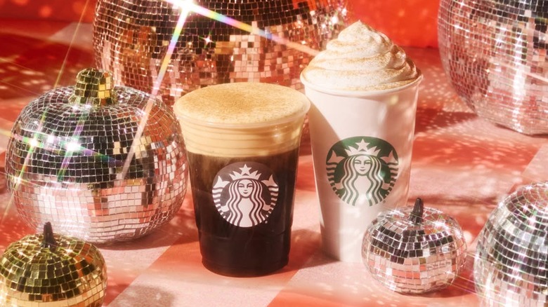 A pumpkin spice latte sits with an iced coffee with pumpkin spice cold foam among disco pumpkins.