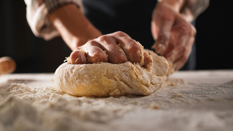 Hands kneading pizza dough on floured surface