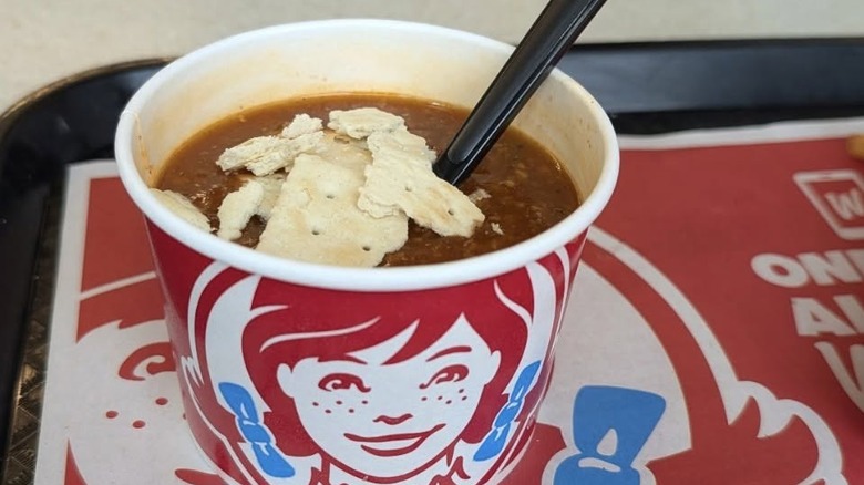 A cup of Wendy's chili with a black spoon and crackers inside
