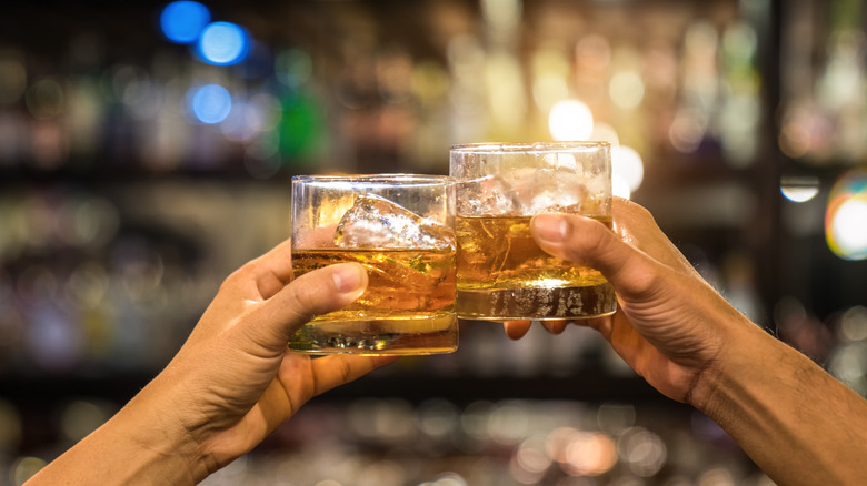two people clinking glasses of whiskey