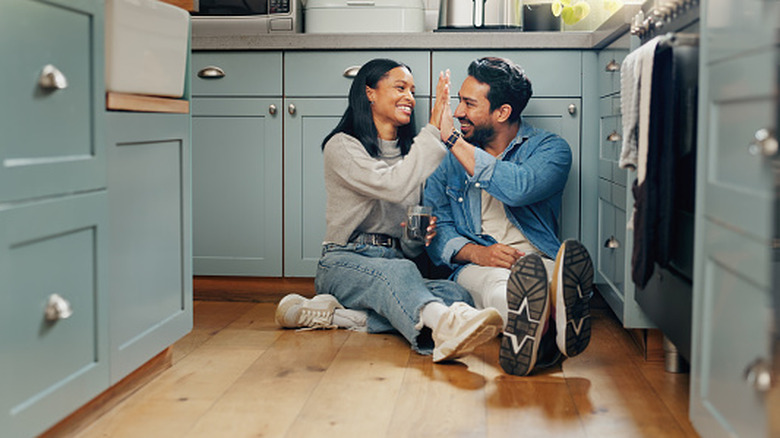 Couple sitting on the kitchen floor drinking coffee and high fiving.