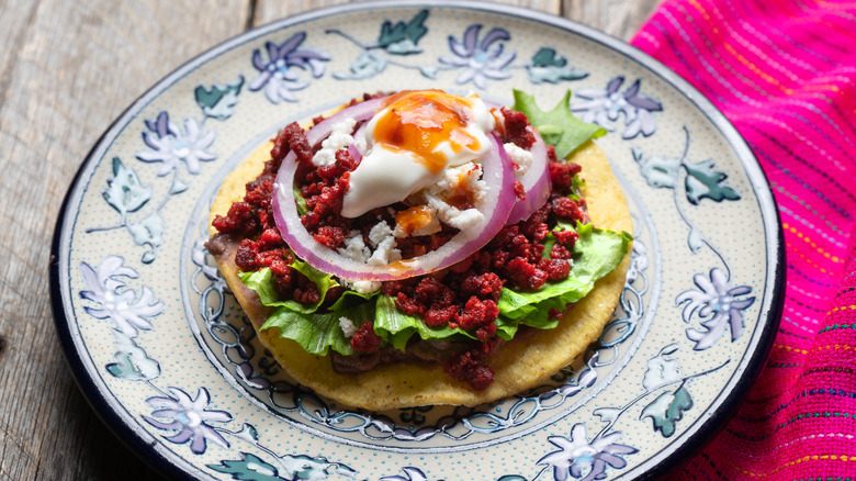 Tostada with chorizo, lettuce, onion, and egg