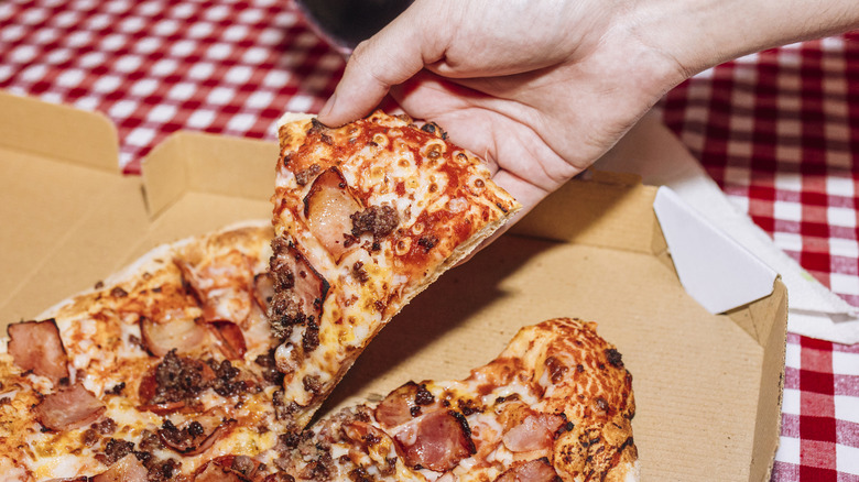 A hand taking a slice of pizza.