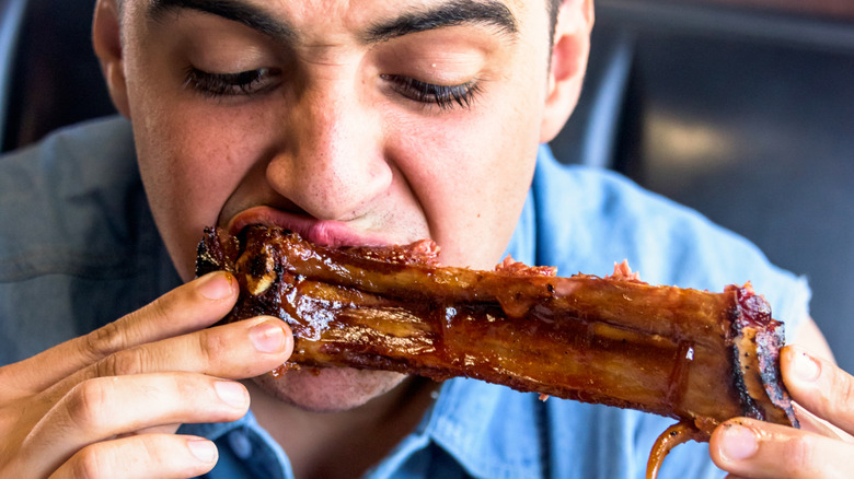 A man awkwardly eats a saucy rib