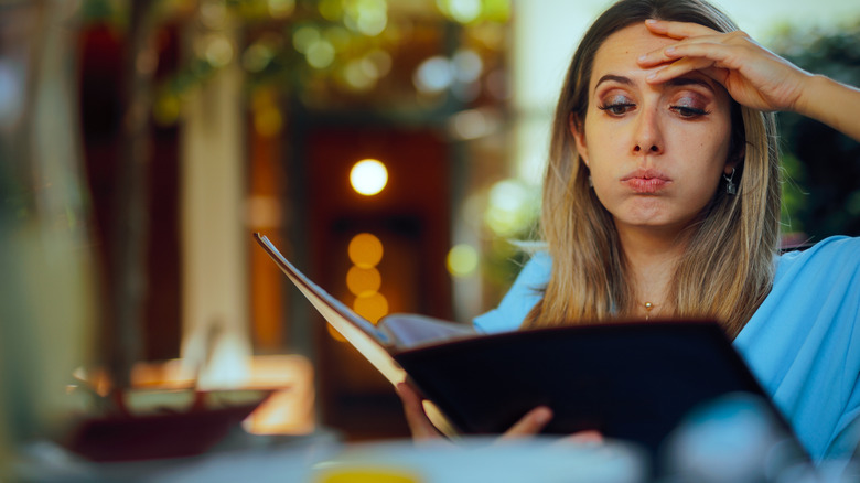 A woman looks stressed and indecisive as she studies a restaurant menu
