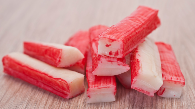 Fresh imitation crab sticks sit in a pile on a wooden surface