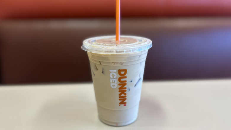 Blueberry iced coffee on a white table in a clear plastic cup with an orange straw and the lid on