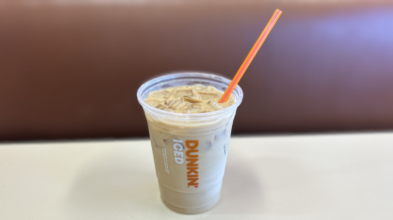French vanilla iced coffee on a white table with the plastic lid off and an orange straw placed in the cup at an angle