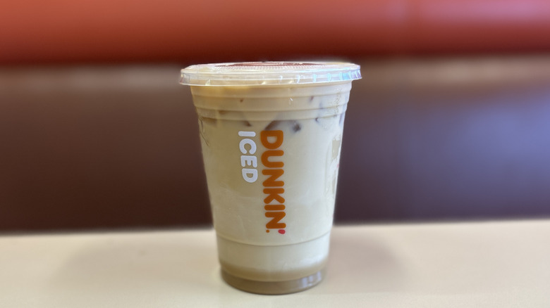Caramel iced coffee on a white table with the plastic lid on top