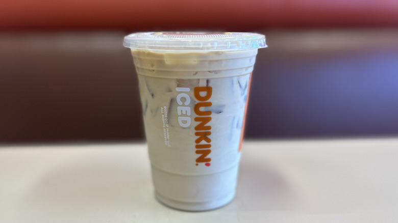 Toasted almond iced coffee on a white table with the plastic lid on top