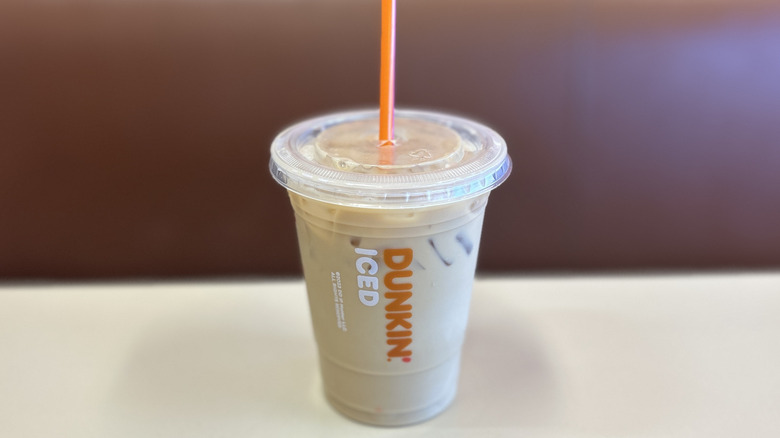 Vanilla iced coffee on a white table in a clear plastic cup with an orange straw and the lid on