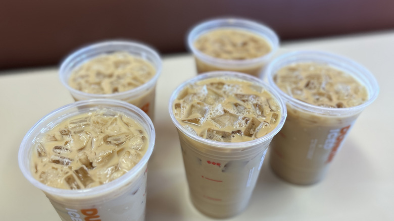 Five Dunkin iced coffees in clear plastic cups on a white table without the lids on