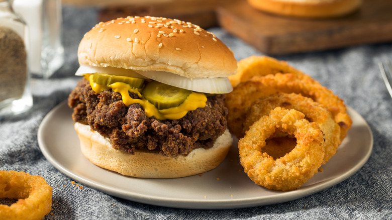 A Mississippi slugburger with pickles, mustard, and onions on a plate with onion rings