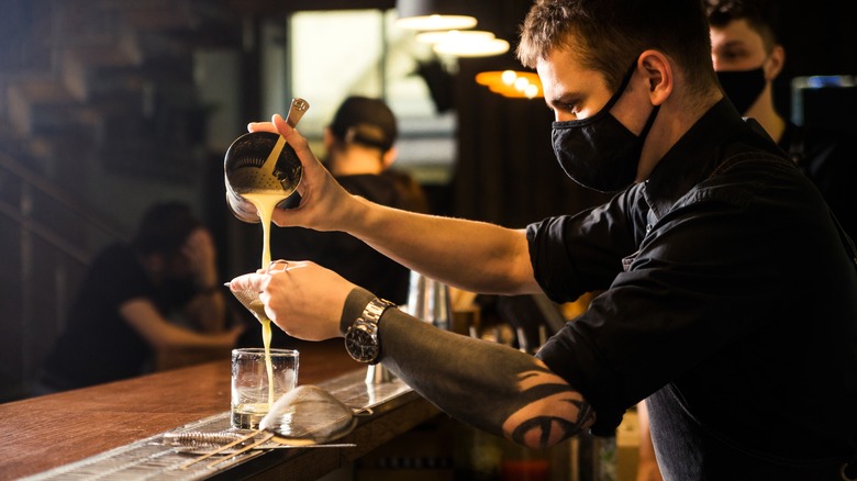 Bartender double straining a whiskey sour