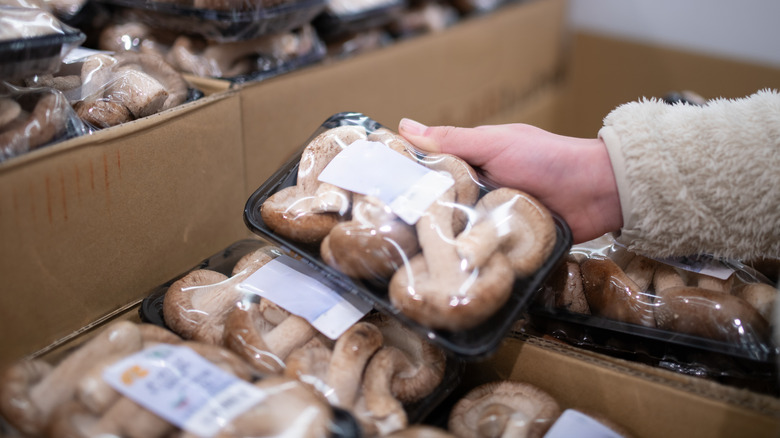Hand selecting a package of mushroom at grocery store