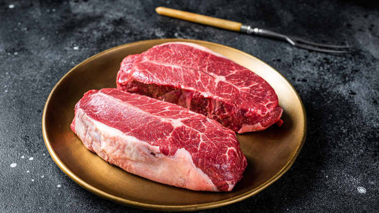 Two flat iron steak cuts on a gold plate placed on a gray tabletop