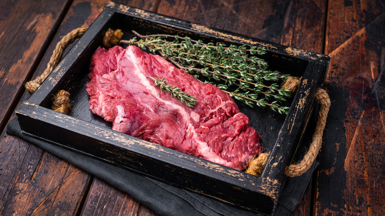 Raw hanger steak on a rustic black rectangular dish placed on a wooden table
