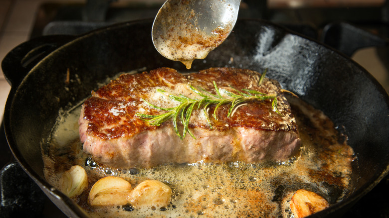 Basting a cut of steak in a black pan with butter and garlic