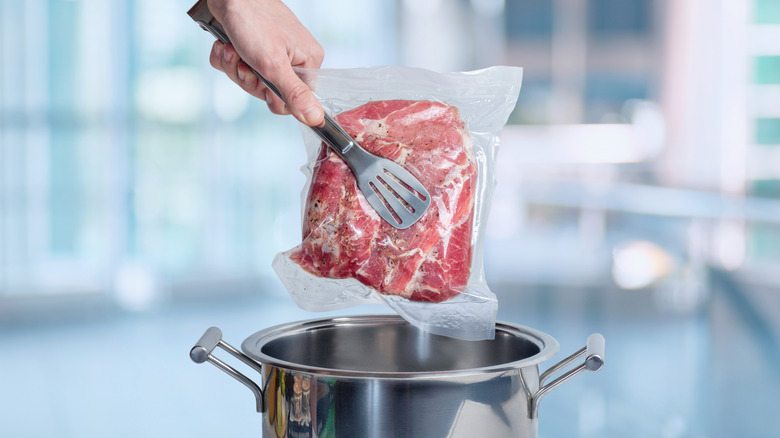 Sous vide steak being held by silver tongs above a metal pot