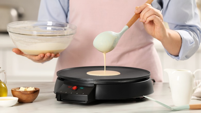 woman pouring crepe batter onto pan