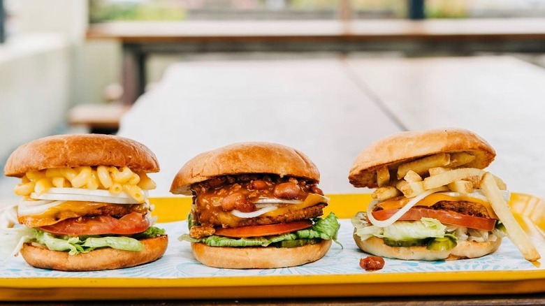 A trio of burgers from Amy's Drive Thru featuring one with organic vegan mac and cheese, chili, and then one topped with french fries