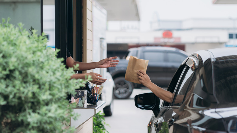 A customer in a black car receives a paper bag of food at a drive-thru