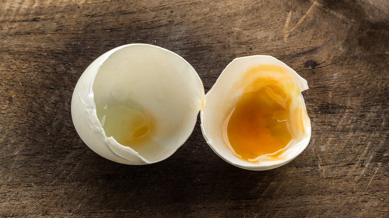 A rotten egg sits cracked open on a wooden surface