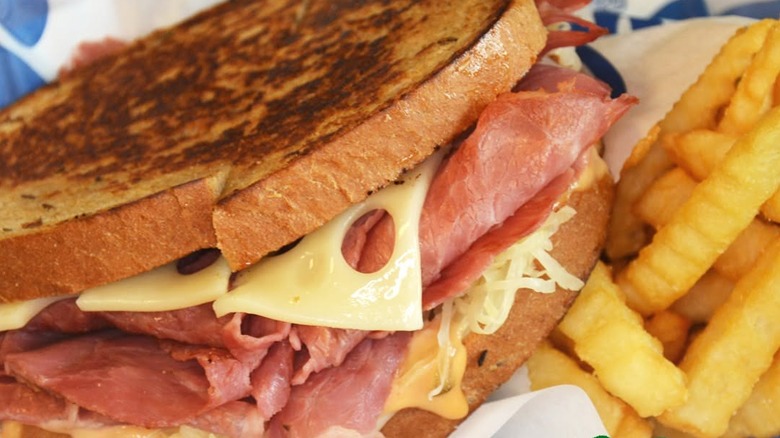 Closeup of a Culver's Grilled Reuben Melt next to a bag of french fries.