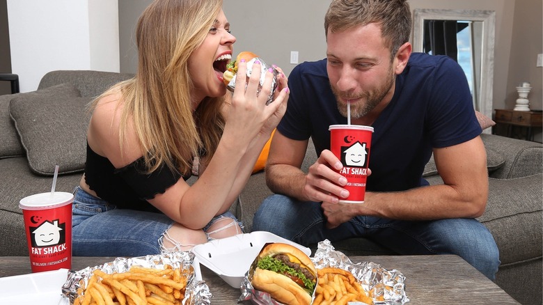 Two diners eat Fat Shack burgers and fries and drink Fat Shack beverages