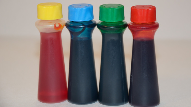 Four bottles of food dye stand side by side against a cream colored background