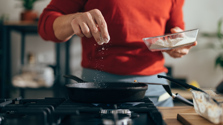 person sprinkling salt into pan