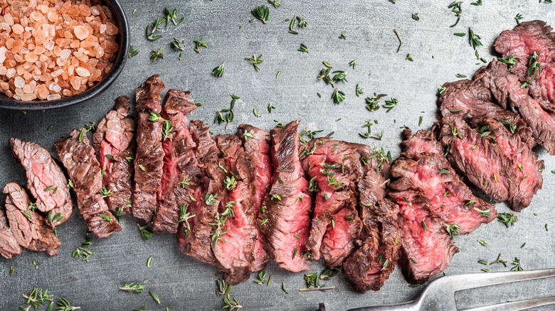 Grilled skirt steak slices on black table with garnish and salt