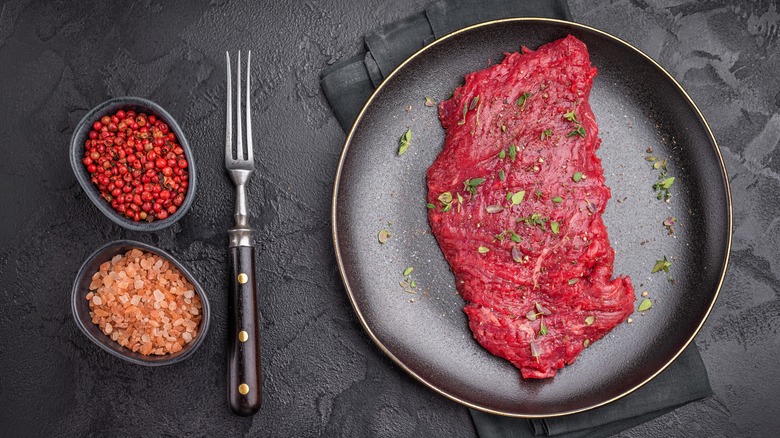 Raw marinated flap meat on black plate with bowls of seasoning