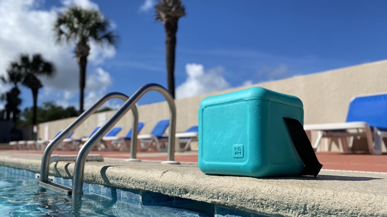A cyan FOAM cooler sits beside a pool and palm trees on a sunny day