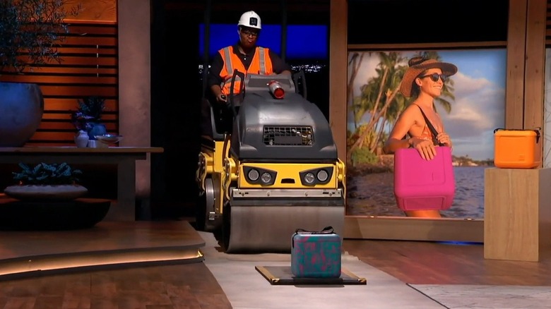 A steamroller enters the "Shark Tank" set and runs over a FOAM cooler