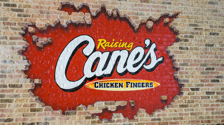 A sign for Raising Cane's Chicken Fingers is painted on a brick wall