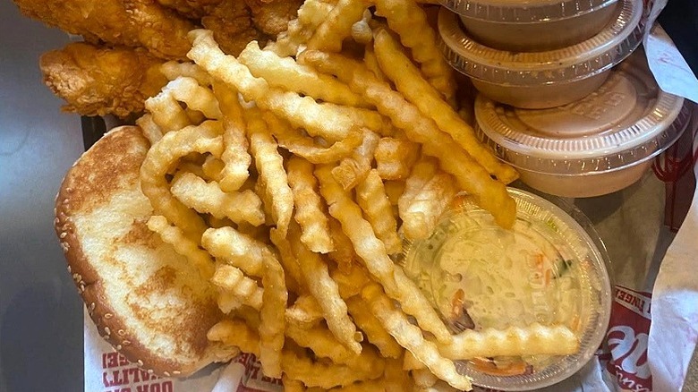 A basket of Raising Cane's fries, slaw, sauce, and bread sit next to chicken tenders