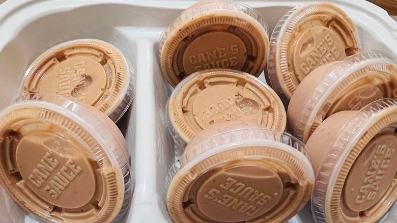 Multiple cups of Cane's Sauce sit in a to-go box