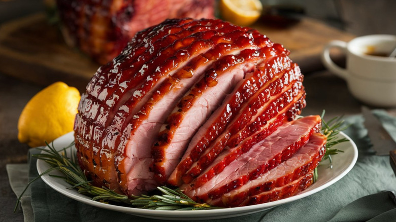 A carved glazed ham with fresh rosemary and lemon wedges.