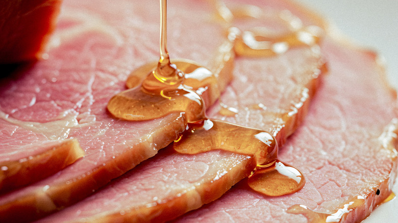 A carved glazed ham has more glaze poured onto it