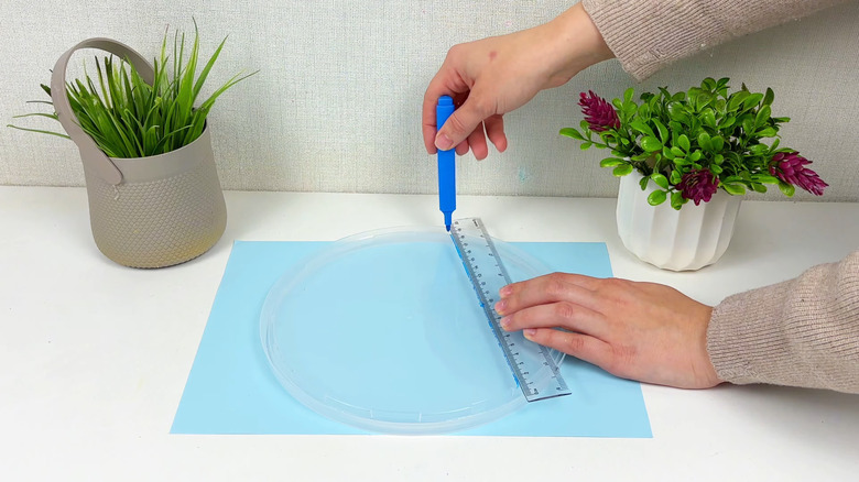 Someone draws lines on a plastic container lid with a ruler and felt tip pen.