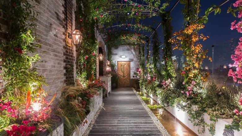 walkway lined with flowers leading to a door with an anchor logo on it
