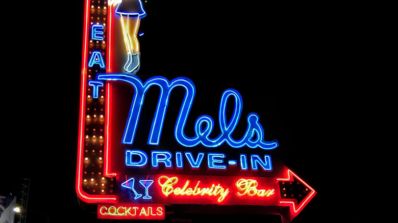 neon mel's drive in diner sign with martini glasses, and the words. "eat", "cocktails", and "celebrity bar" with an arrow