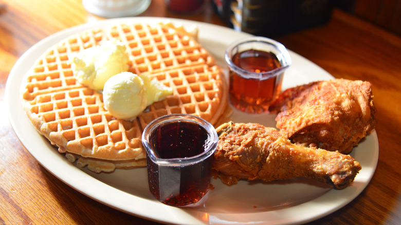 plate of waffles, two pieces of fried chicken, and syrup on top of a brown table